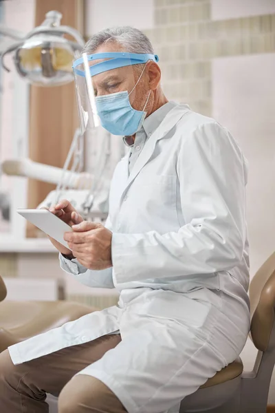 Vážný zubní specialista pracující na svém tabletu — Stock fotografie