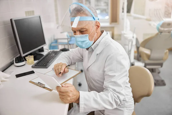 Médico de edad avanzada enfocado comprobar los datos en su comprimido — Foto de Stock