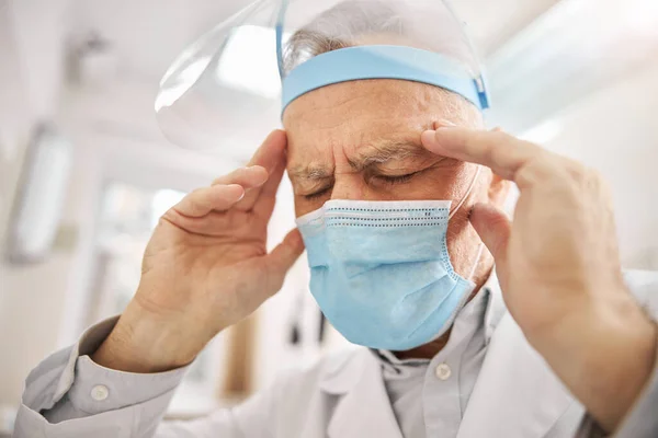 Elderly healthcare professional touching his head and frowning — Stock Photo, Image