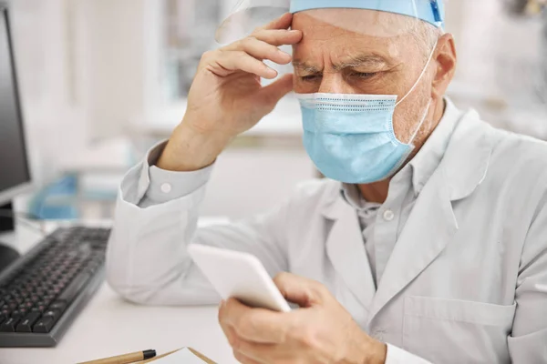Åldrad läkare tittar på sin smartphone — Stockfoto