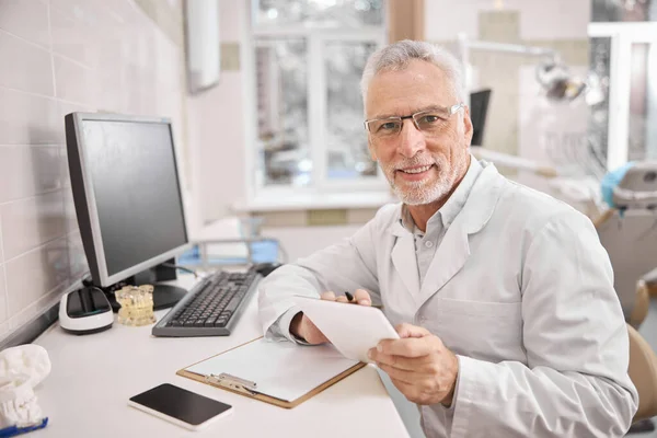 Amichevole medico anziano seduto alla scrivania del suo ufficio — Foto Stock