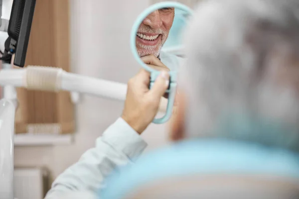 Paciente de pelo gris mirando su sonrisa en el espejo — Foto de Stock