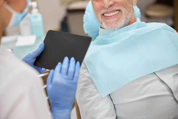Starszy pan uśmiechający się do dentysty trzymającego tablet — Zdjęcie stockowe