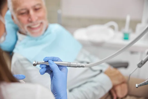 Odontólogo cualificado que sostiene un taladro dental para tratar a un paciente — Foto de Stock