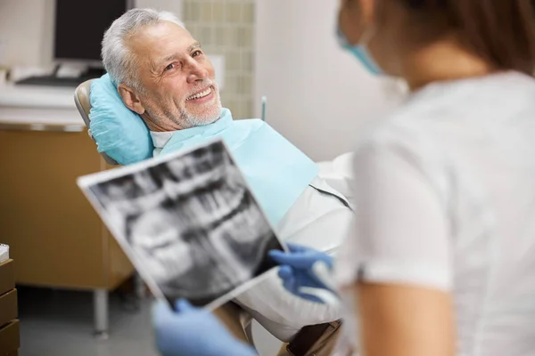 Idős polgár, aki fogorvosi székben ül, és egy fogtechnikusra néz. — Stock Fotó