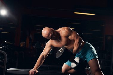 Spor salonunda dambılları kaldıran kaslı adam.