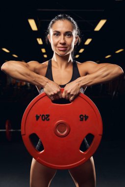 Kaslı bayan sporcu iki eliyle ağırlık kaldırıyor.