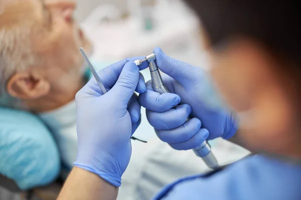 Dentista con guantes de látex sosteniendo un bruñidor dental — Foto de Stock