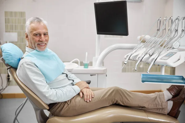 Vidám idős férfi ül egy fogorvosi székben — Stock Fotó