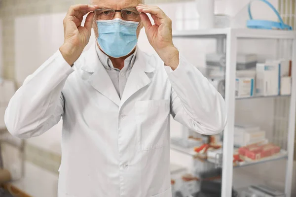 Serieuze gezondheidswerker in een labjas zet bril op — Stockfoto