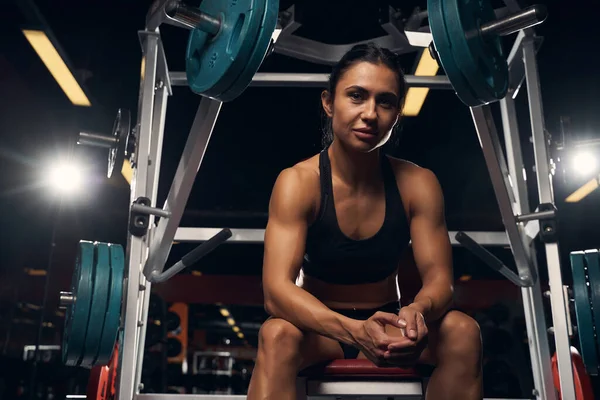 Muscled ung dam vilar nära en smed maskin på gymmet — Stockfoto