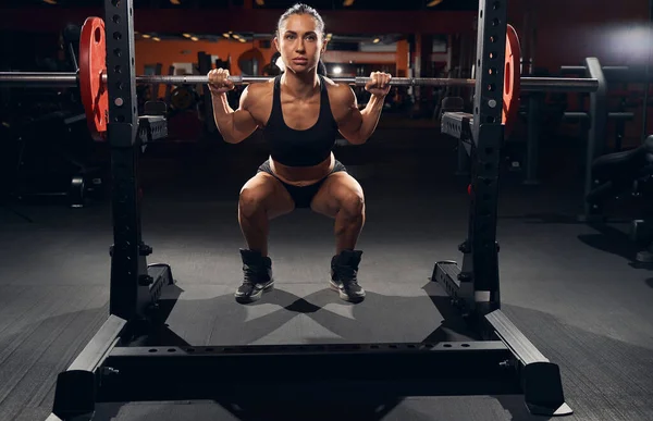 Sterke vrouwelijke atleet doet squats met een lange halter — Stockfoto