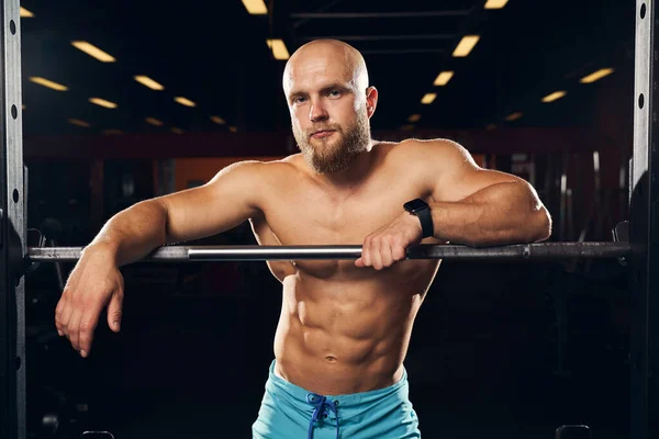 Deportista musculoso de pie junto a una barra en el gimnasio —  Fotos de Stock