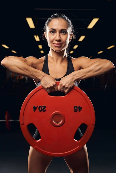 Musculosa atleta femenina levantando placa de peso con ambas manos — Foto de Stock