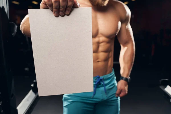 Sporty shirtless male holding an empty paper sheet — Stock Photo, Image