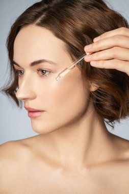 Çekici bir genç kadın yüzüne vitamin serumu sürüyor.