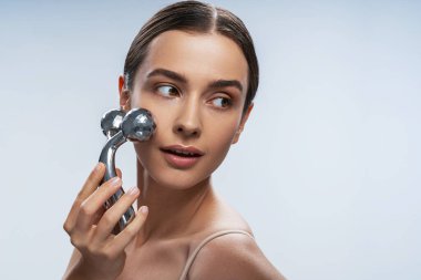 Platin yüz masajı aleti kullanan çekici genç bir kadın.