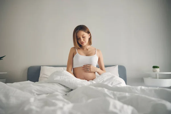 Aantrekkelijke zwangere vrouw zittend in wit bed — Stockfoto