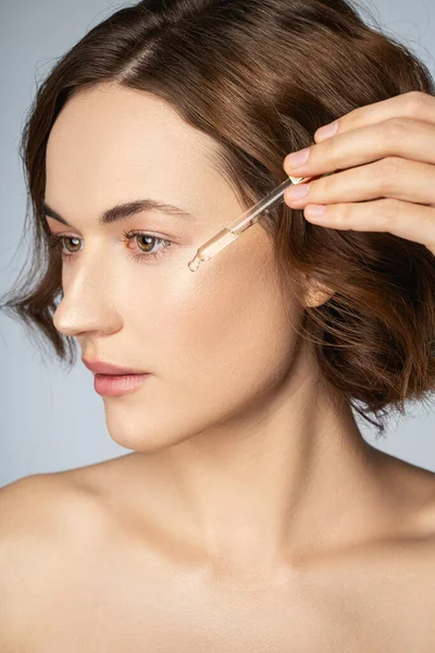 Charming young woman applying vitamin serum on her face — Stock Photo, Image