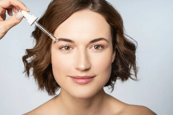 Kadın eli, kadın yüzüne vitamin serumu sürüyor.