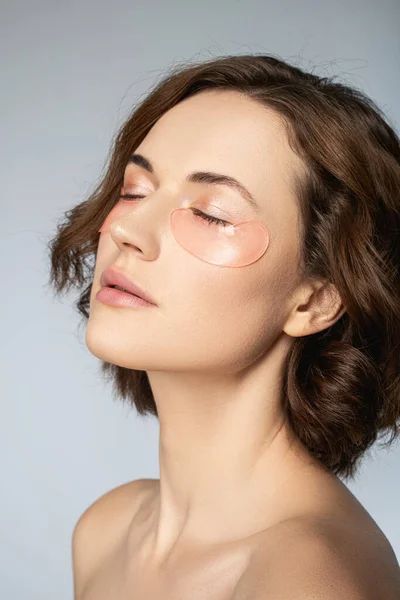 Jeune femme sereine avec une peau parfaite en utilisant des patchs sous les yeux — Photo