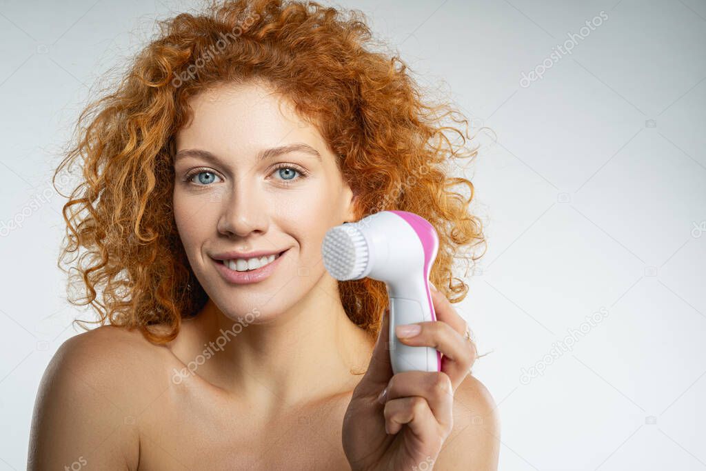 Joyful young woman holding cleansing face brush
