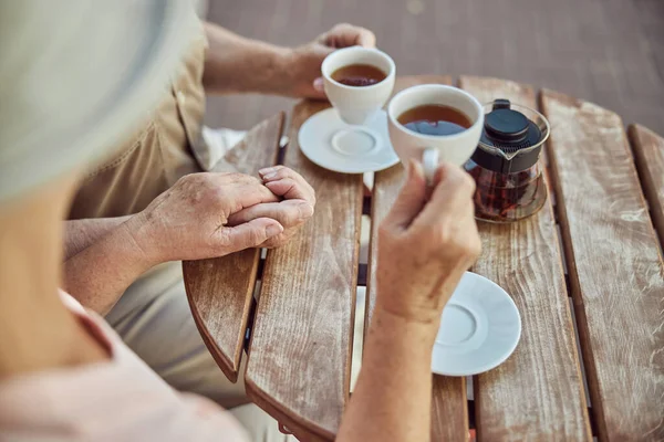 Oudere echtpaar drinken thee aan een houten tafel buiten — Stockfoto