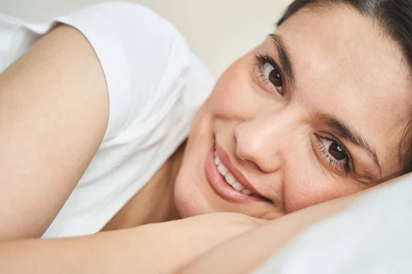 ベッドに横たわっリラックスした暗い髪の女性の笑顔 — ストック写真