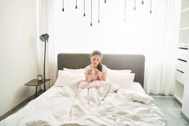 Depresyondaki genç beyaz kadın yatakta oturuyor.