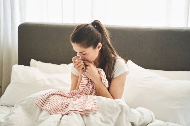 Neşesiz, siyah saçlı, yatakta yalnız oturan kadın.