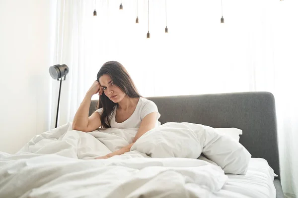 Overstuur jonge langharige vrouw zittend in bed — Stockfoto