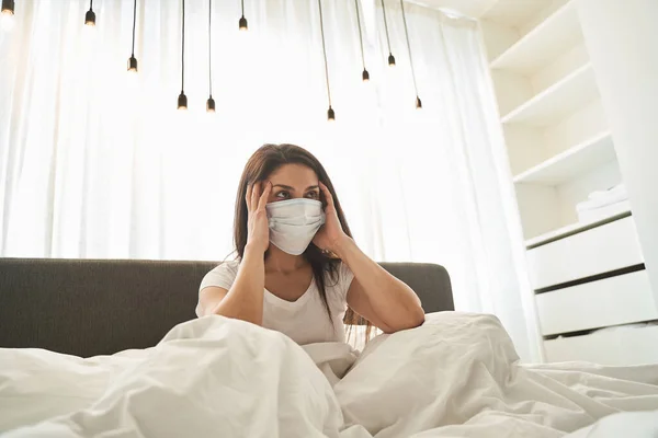 Baş ağrısı olan hasta bir kadın yatakta oturuyor. — Stok fotoğraf