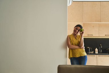 Gözleri kapalı neşeli bir kadın, elinde elma tutuyor.