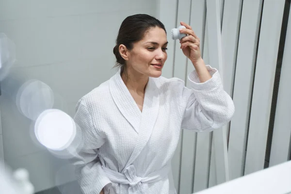 Señora enfocada usando un cepillo de limpieza facial — Foto de Stock