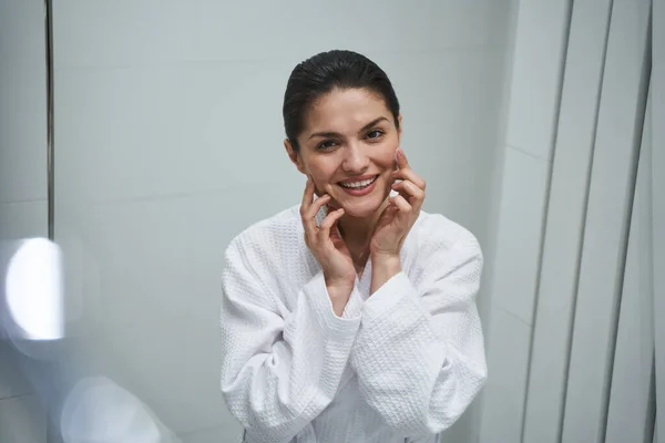 Lächelnde Frau reibt eine Gesichtscreme in ihre Haut — Stockfoto