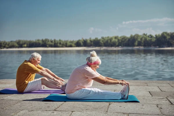Dois iogues iniciantes seniores realizando um exercício de alongamento — Fotografia de Stock