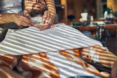 Kaslı gömlekli esmer adam tıraş oluyor.