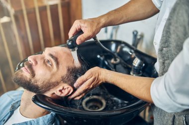 Berber dükkanının soğuk, genç müşterisi saç yıkıyor.