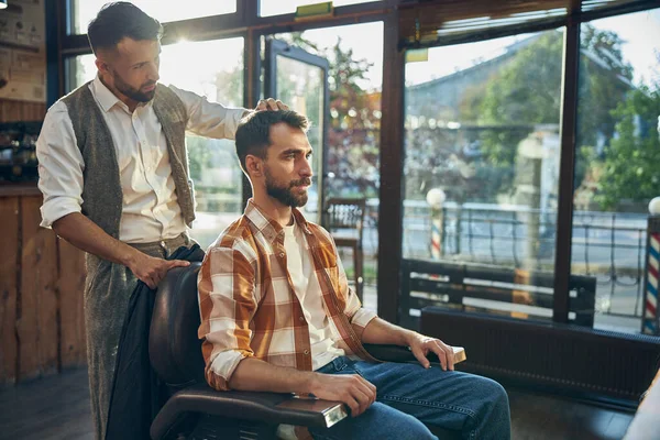 Kvalifikovaný holič dotýkající se vlasů svého klienta v salonu — Stock fotografie