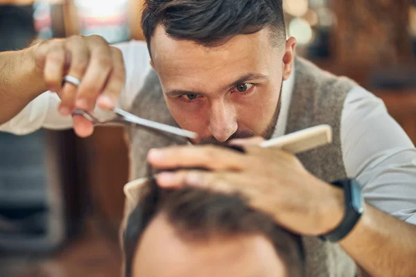 Geconcentreerde kapper op zoek naar het haar van een klant tijdens een kapsel — Stockfoto