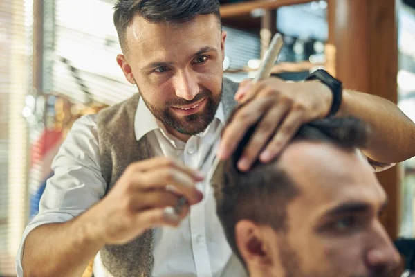 Alegre cabeleireiro dando a seu cliente um corte de cabelo — Fotografia de Stock