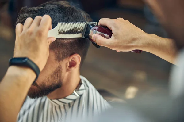 Estilista hábil usando un cortador de pelo eléctrico para cortar el cabello — Foto de Stock