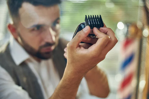 プロの理容師は電動ヘアトリマーを注意深く見て — ストック写真