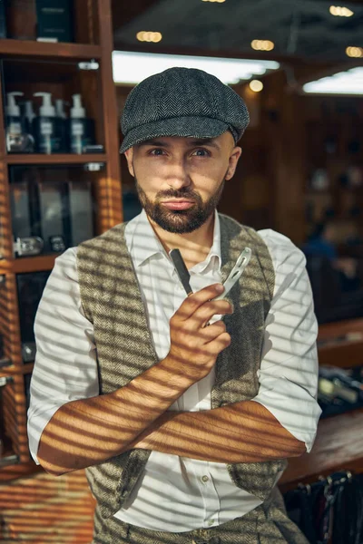 Serious hairdresser holding a razor and posing in a salon — Stock Photo, Image