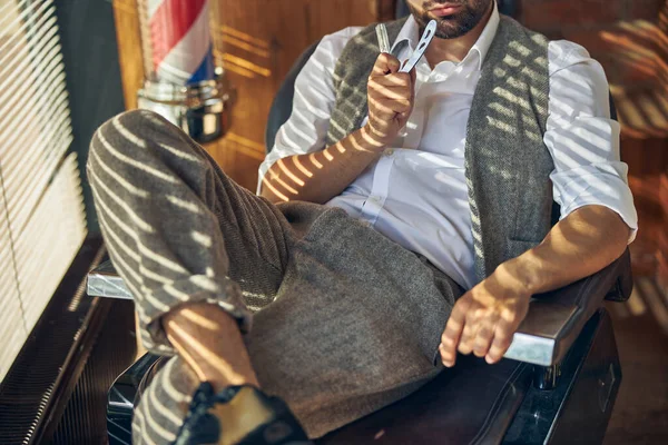 Peluquero vestido elegante descansando en un sillón sosteniendo una navaja de afeitar —  Fotos de Stock