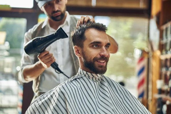 Bir kuaförde saçları kuruyan neşeli, esmer bir adam.