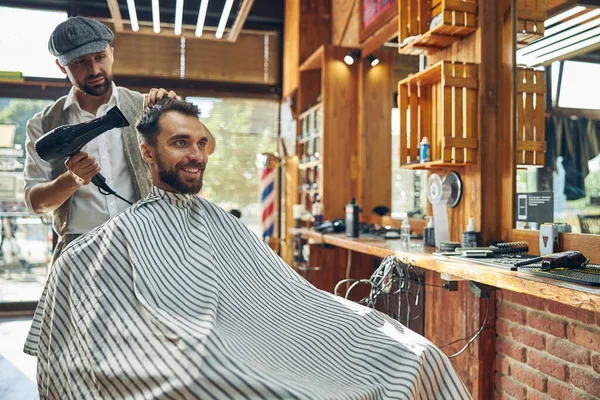 Веселый молодой человек, высушивающий волосы в парикмахерской — стоковое фото