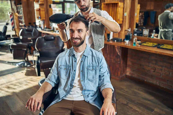 Berber dükkanının neşeli müşterisi saçını fön çektirmiş.