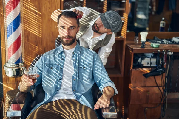 Entspannter junger Mann bei einem Glas Whisky beim Friseur — Stockfoto