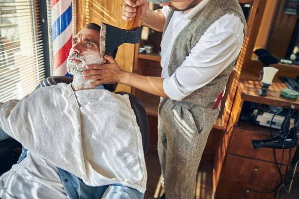 Парикмахер работает топором во время бритья своего клиента — стоковое фото